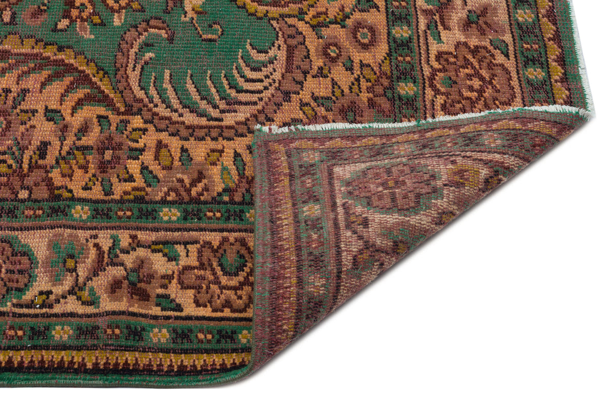 Green and brown traditional rug with an ornate floral pattern, shown with a corner folded over on a white background.