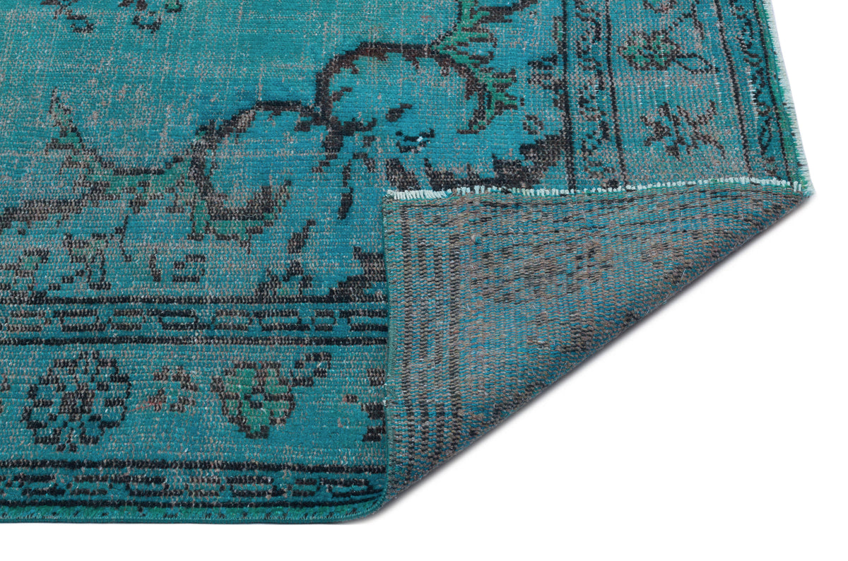 Teal and charcoal distressed rug with a traditional floral medallion pattern, shown with a folded corner.