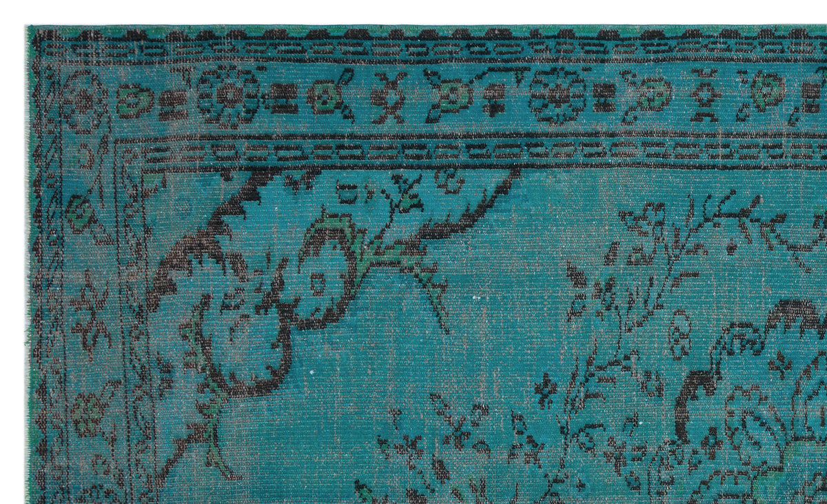 Teal rug with a distressed black floral medallion pattern and a decorative geometric border.