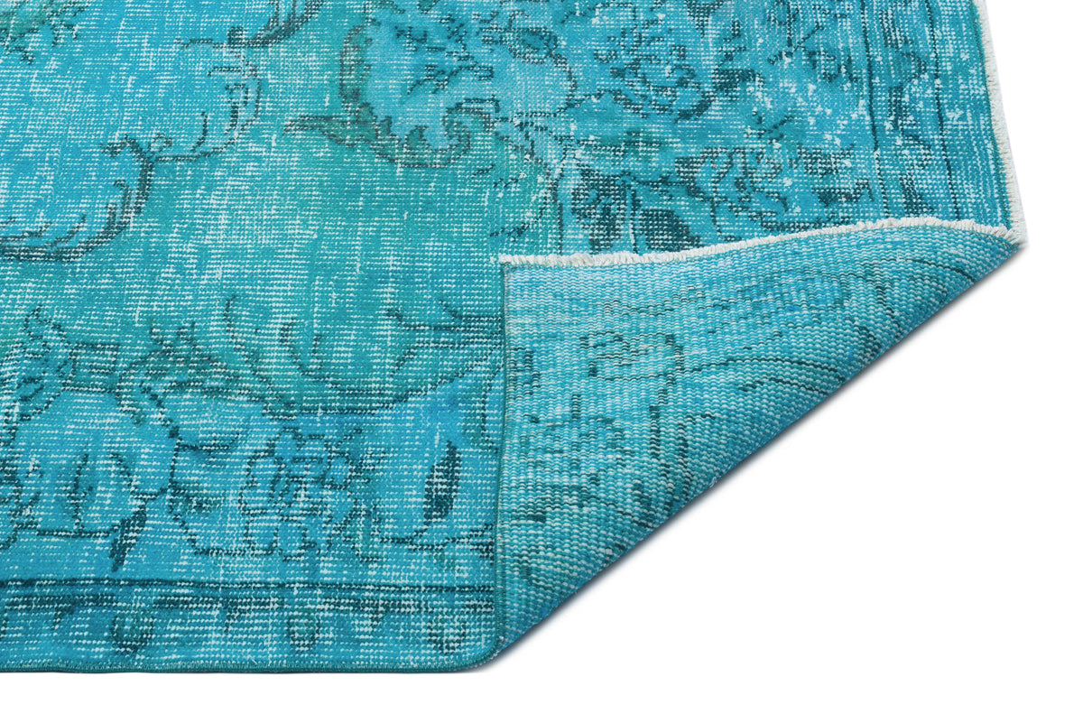 Bright turquoise distressed rug with a faded traditional floral pattern and a folded corner, on a white background.