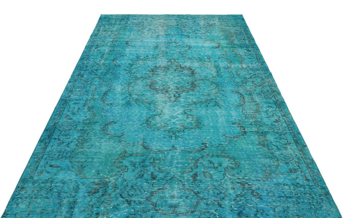 Distressed turquoise rug with a faded dark floral medallion pattern on a white background.
