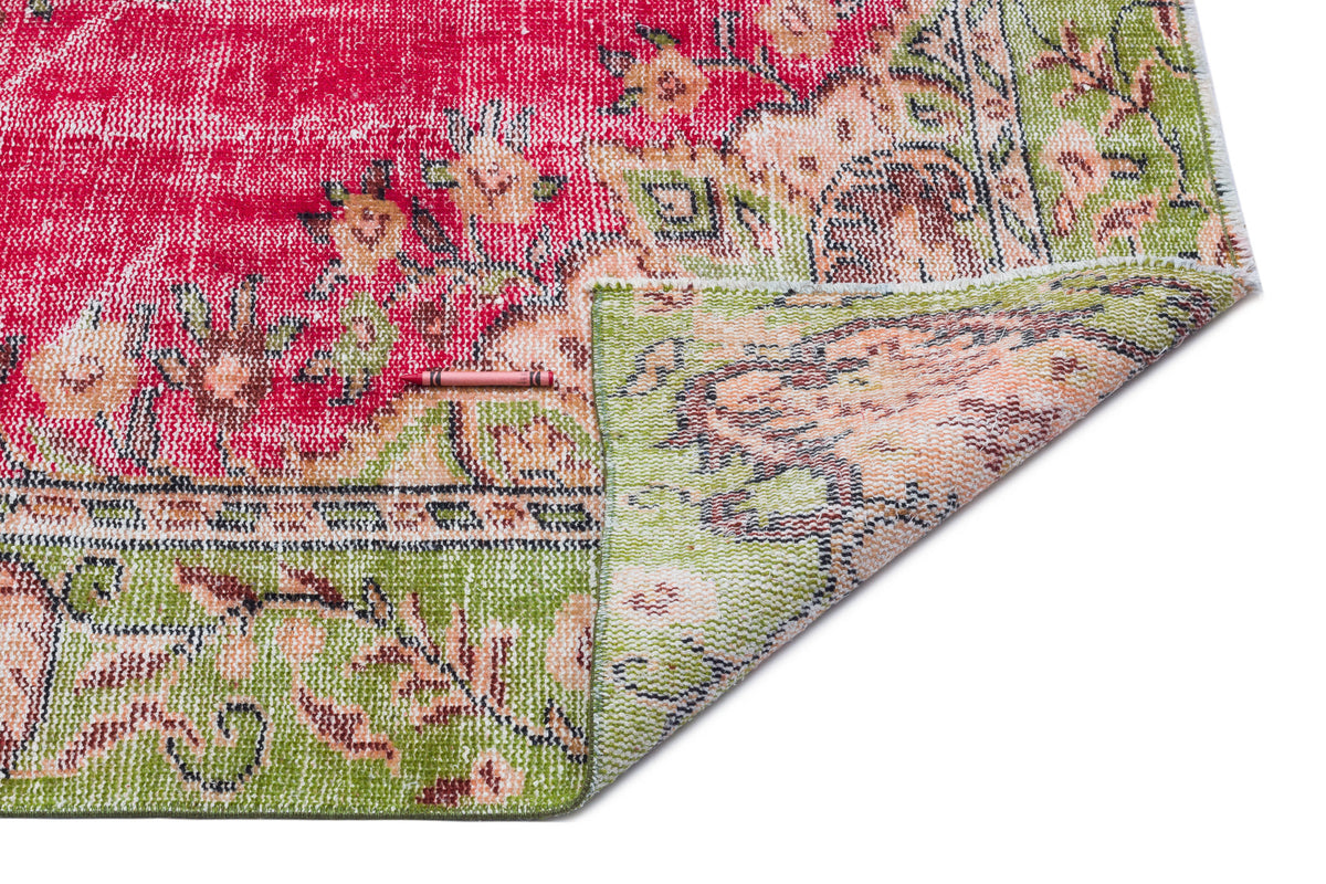 Distressed red and green floral medallion rug with a folded corner on a white background.