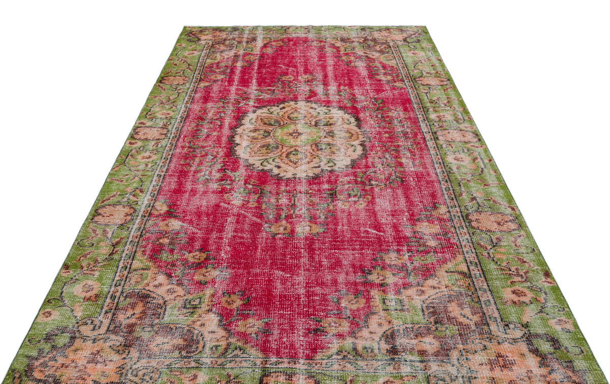 Distressed magenta and green vintage-style rug with a central floral medallion and ornate border on a white background.