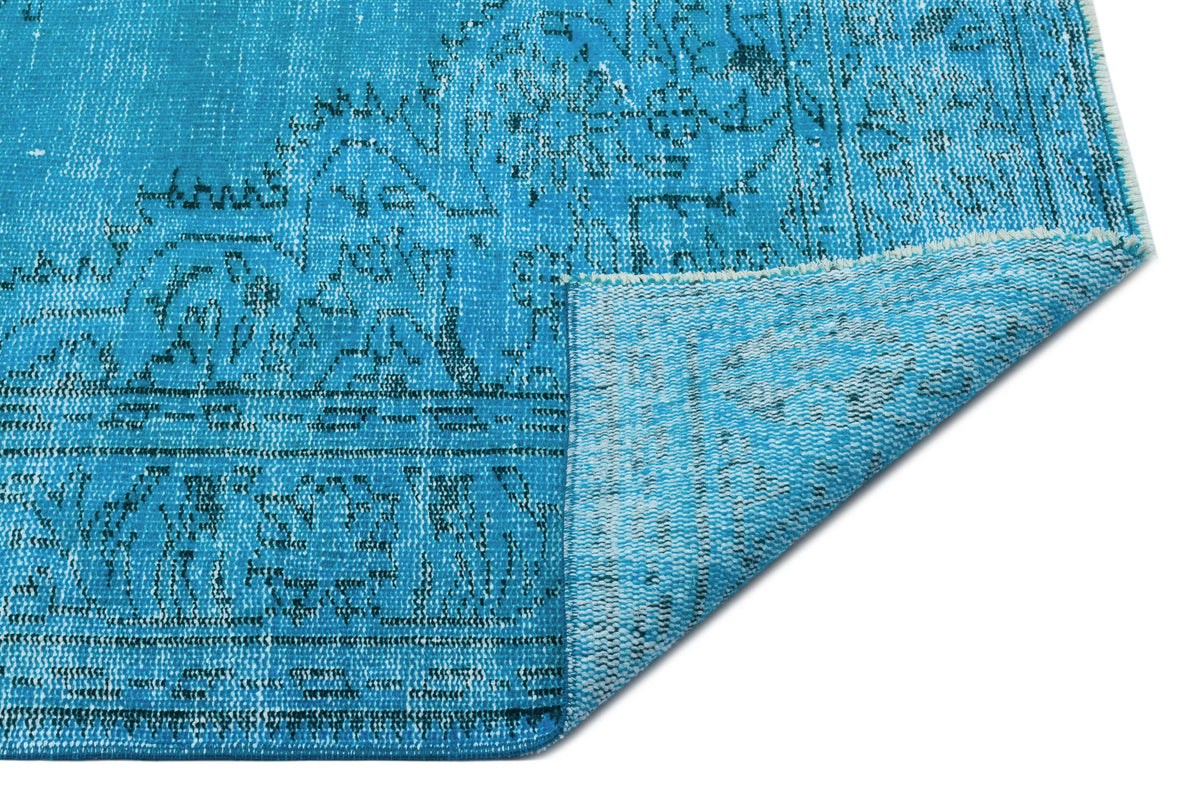Bright turquoise distressed rug with a dark blue traditional medallion pattern, shown with a folded corner.