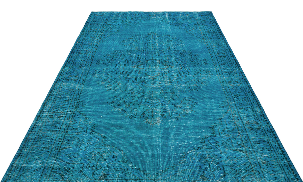 Bright turquoise distressed rug with a dark blue traditional medallion pattern on a white background.