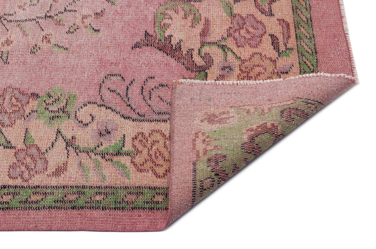 Distressed pink rug with green and brown floral patterns and a folded corner revealing the woven backing.