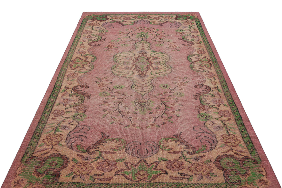 Pink vintage-style rug with a central floral medallion and green and brown ornate border patterns on a white background.
