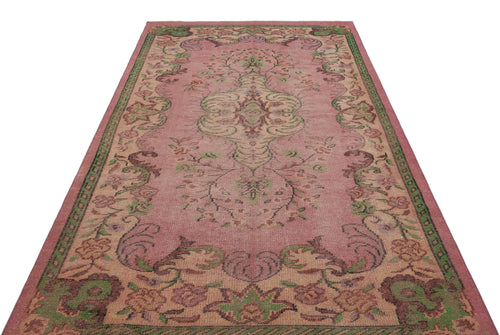 Load image 1 in gallery view. Pink vintage-style rug with a central floral medallion and green and brown ornate border patterns on a white background.