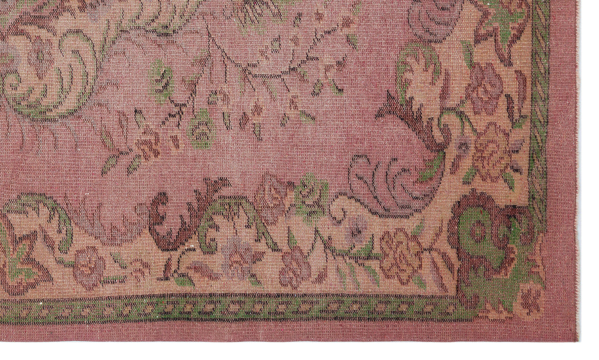 Dusty rose rug with a distressed floral pattern in green and dark brown, featuring a decorative border.
