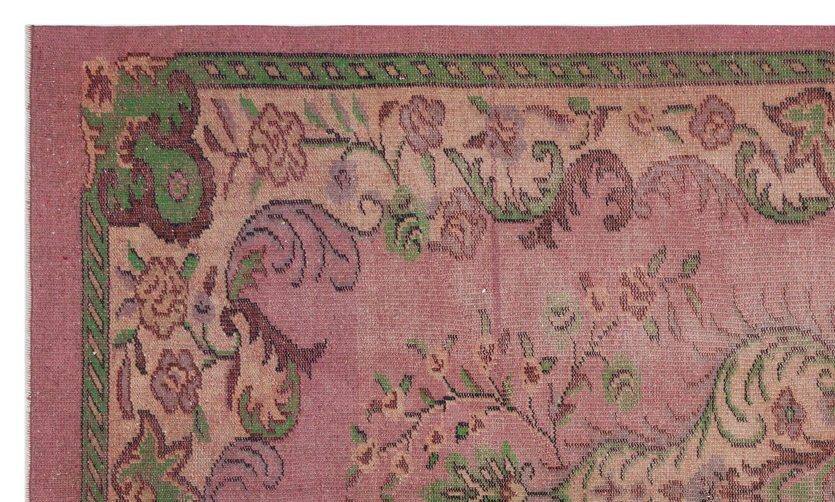 Dusty rose rug with a green and brown floral border and traditional Persian-style botanical motifs.