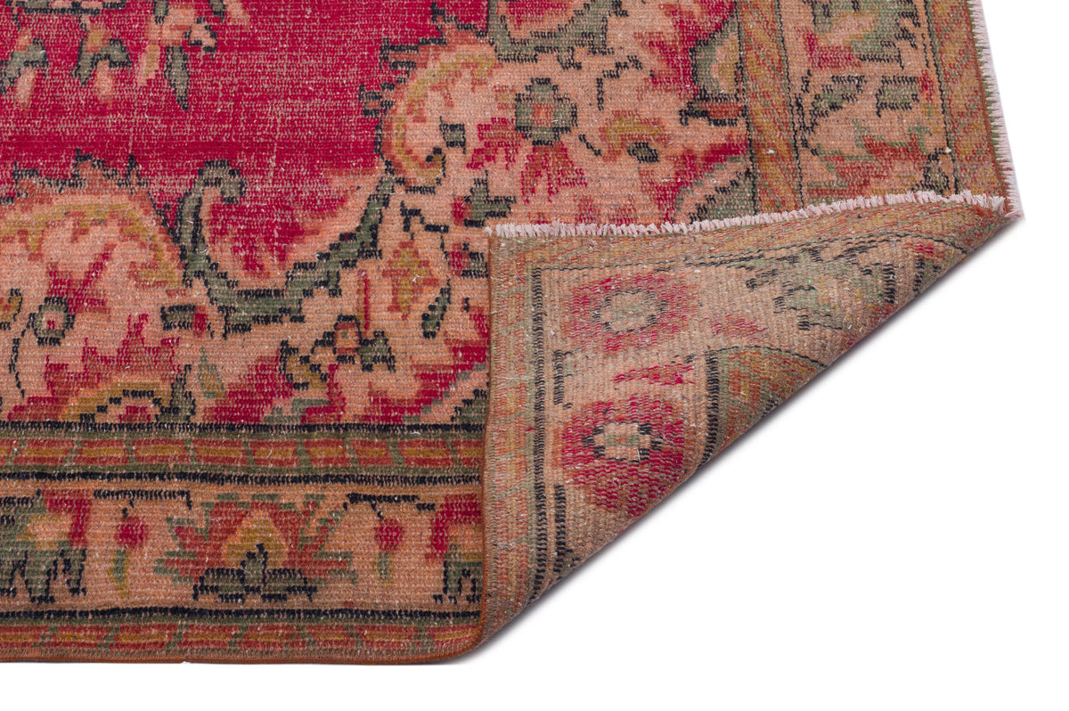 Red and peach vintage-style rug with a floral medallion pattern and a folded corner showing the underside.