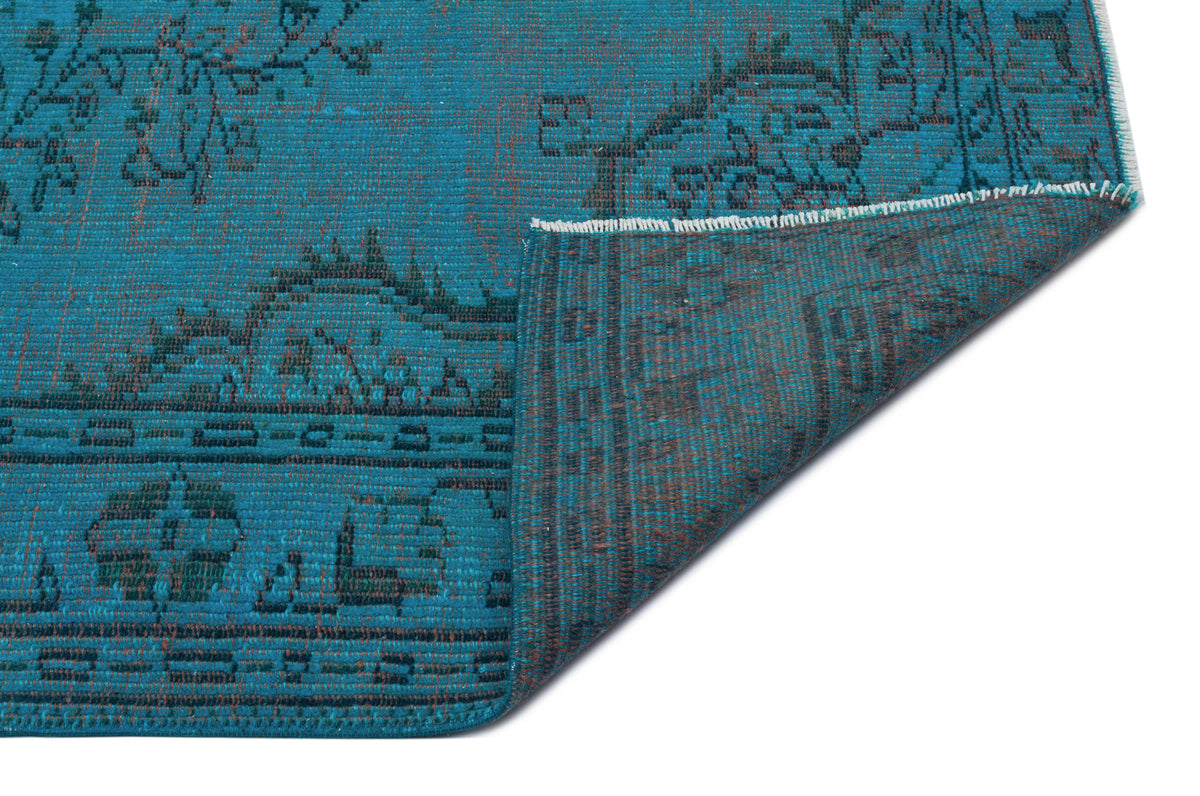 Teal rug with a dark distressed floral medallion pattern, shown with a corner folded over on a white background.