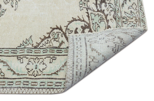 Load image 1 in gallery view. Beige, brown, and sage green vintage-style rug with a floral medallion pattern, shown with a corner folded over.