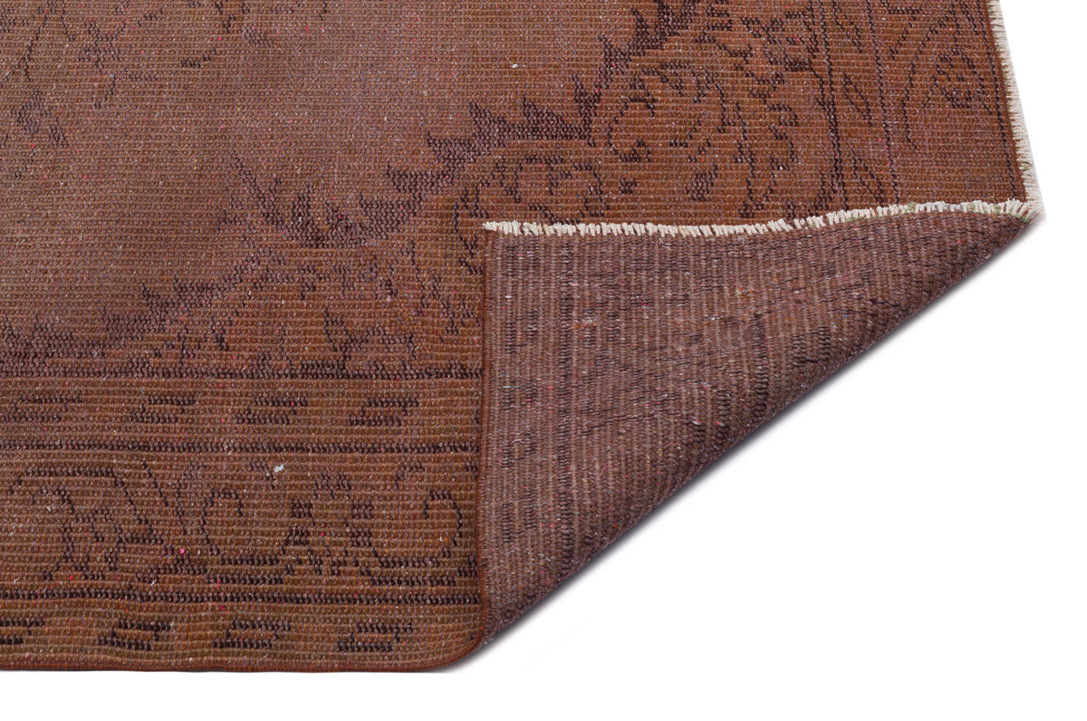 Rust-brown vintage rug with a faded floral border and a corner folded over to reveal the woven backing.