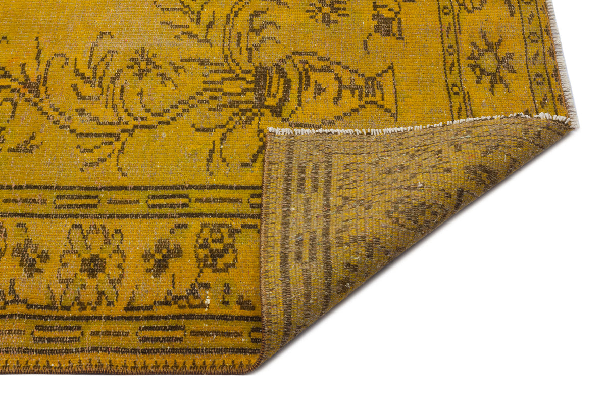Mustard yellow vintage-style rug with dark brown floral motifs and a folded corner revealing the woven backing.