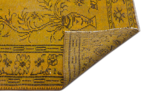 Load image 1 in gallery view. Mustard yellow vintage-style rug with dark brown floral motifs and a folded corner revealing the woven backing.