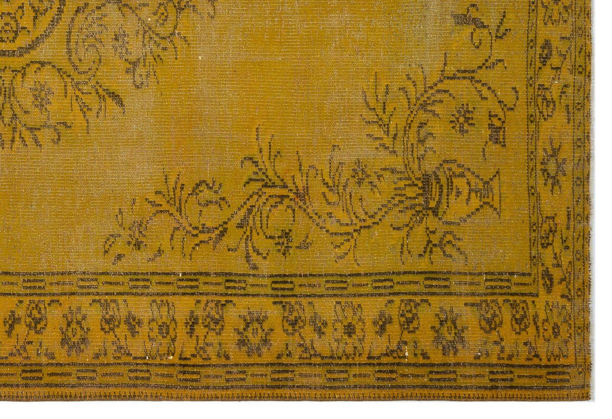 Mustard yellow rug with a dark brown floral and urn motif and a decorative geometric border.