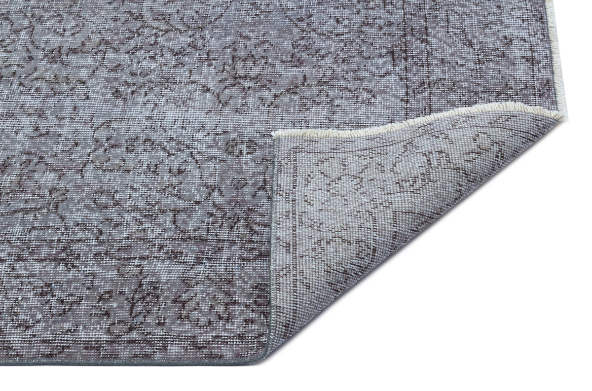 Grey and brown distressed traditional rug with a floral medallion pattern, shown with a corner folded over.