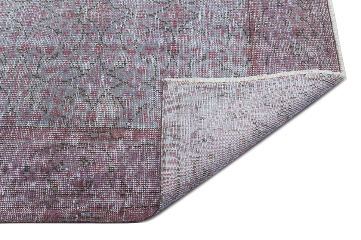 Distressed mauve and grey rug with a faded floral medallion pattern, shown with a corner folded to reveal the backing.