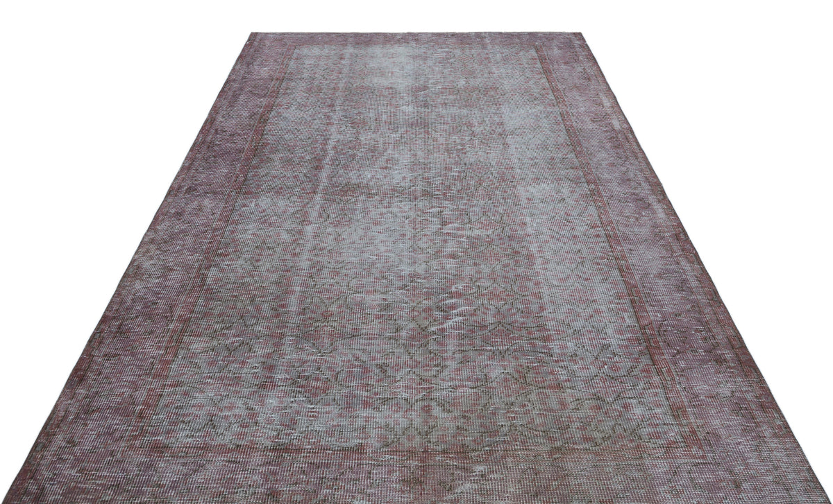 Faded mauve and grey vintage-style rug with a distressed floral medallion pattern and a wide border.