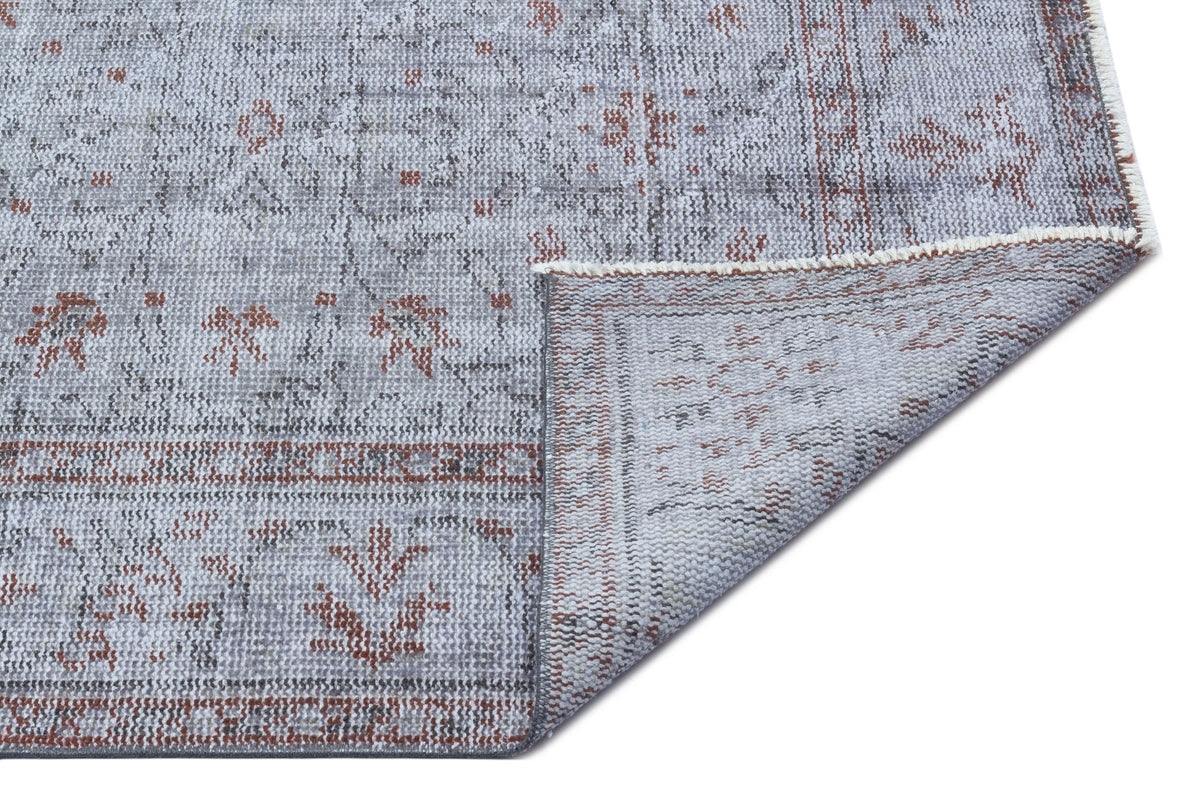 Grey and rust-colored distressed rug with a traditional medallion pattern and a folded corner showing the backing.