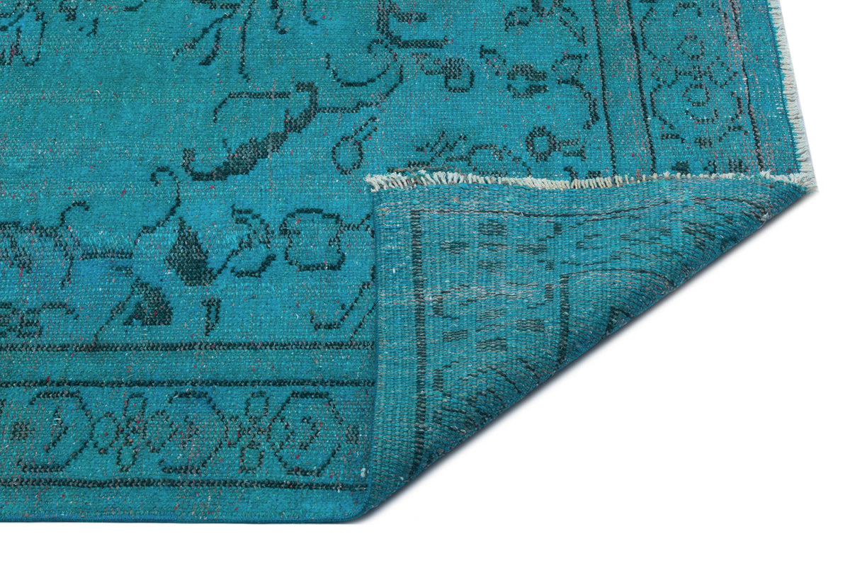 Teal rug with a black traditional floral pattern and a folded corner showing the woven backing.