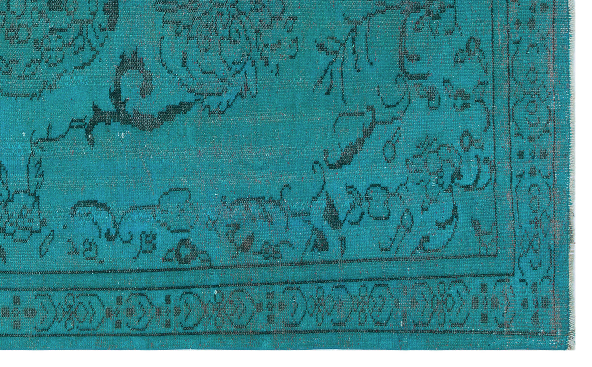 Teal rug with a black distressed floral medallion pattern and a geometric border.