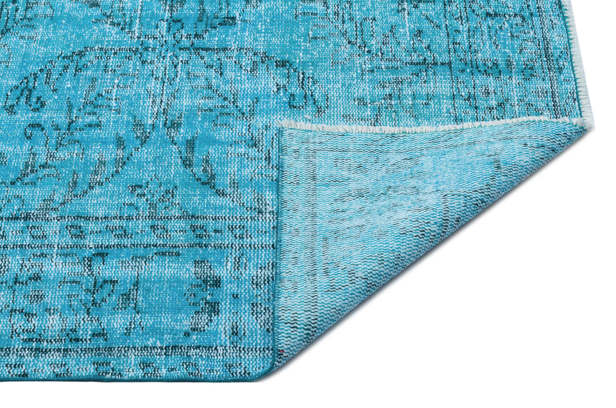 Bright turquoise rug with a distressed traditional medallion pattern, shown with a corner folded over on a white background.