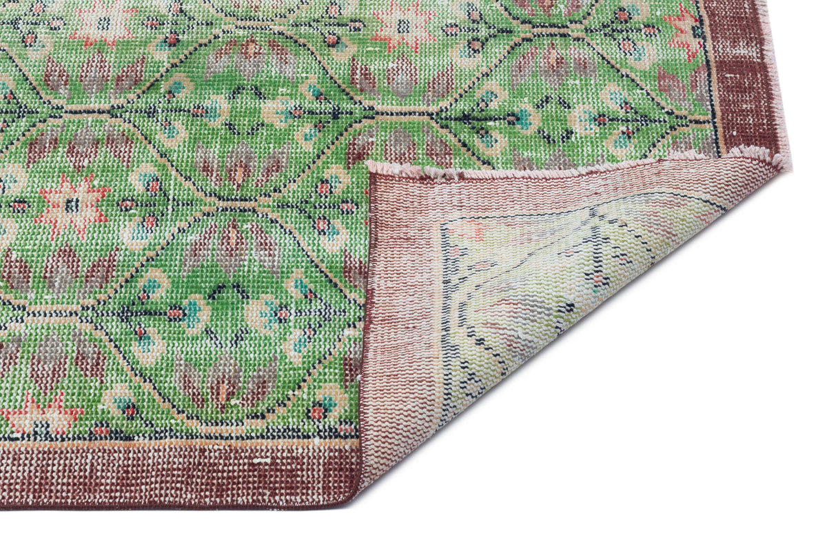Green and maroon vintage-style rug with a floral medallion pattern and a folded corner showing the woven backing.
