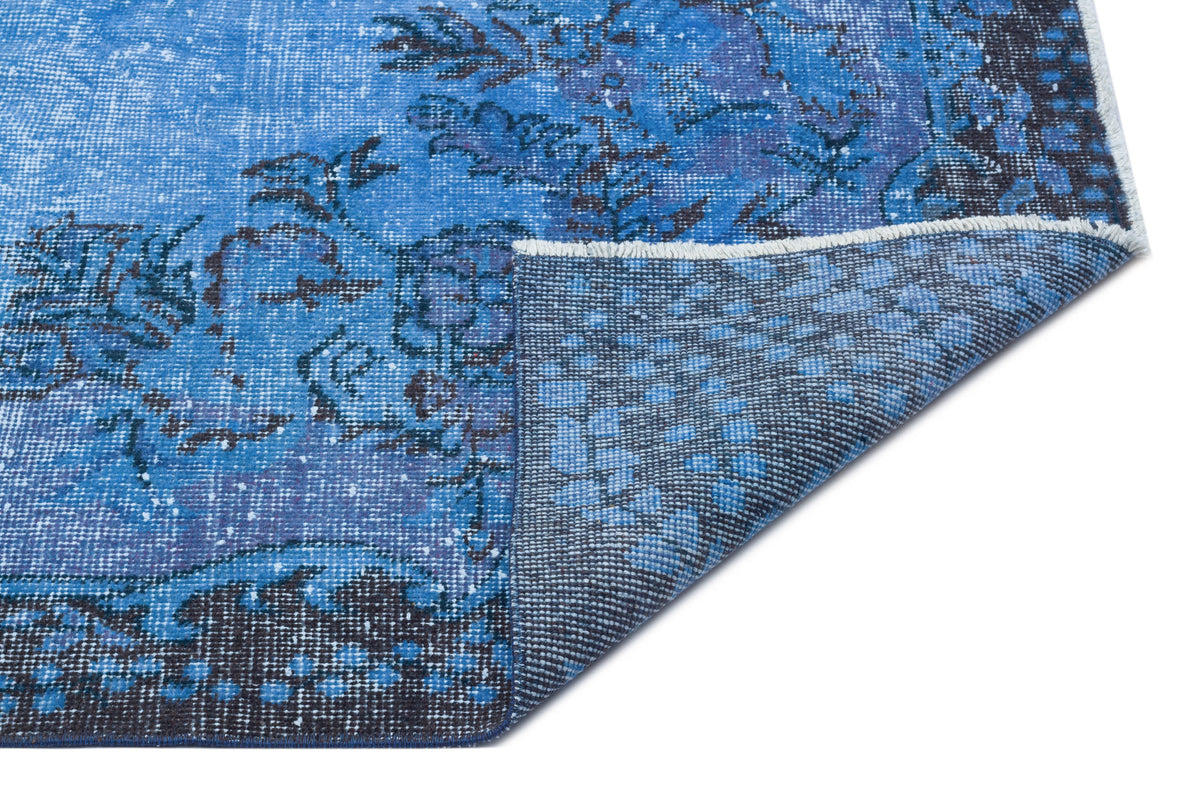 Blue and dark grey distressed floral medallion rug with a folded corner showing the woven backing.
