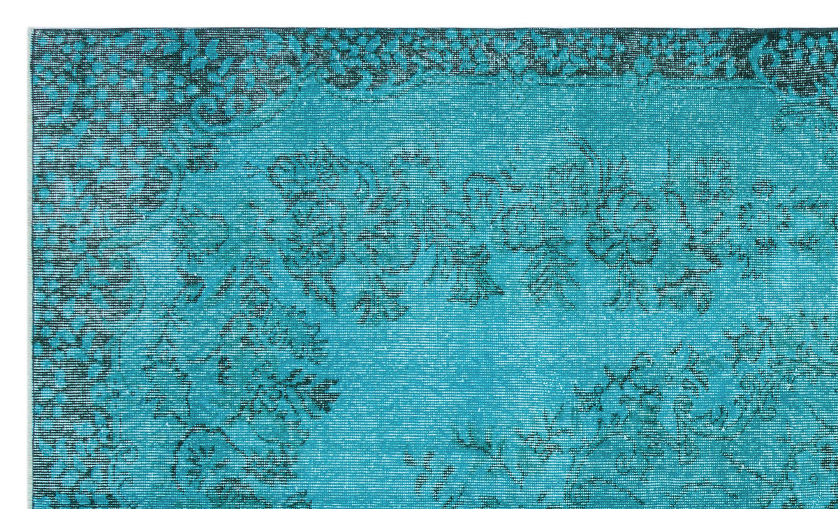 Teal rug with a distressed black floral pattern and a decorative border.