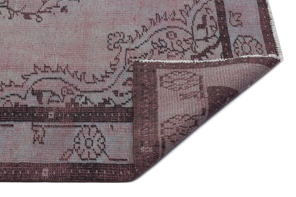 Muted mauve and dark brown traditional rug with a floral medallion pattern, shown with a corner folded over.