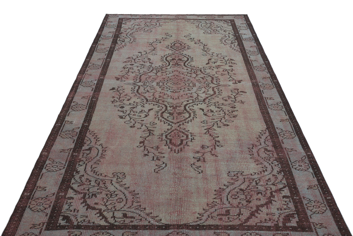 Faded pink and brown vintage-style rug with a central floral medallion and a decorative border.