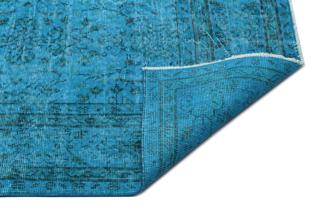 Bright turquoise rug with a distressed traditional medallion pattern and a folded corner showing the backing.
