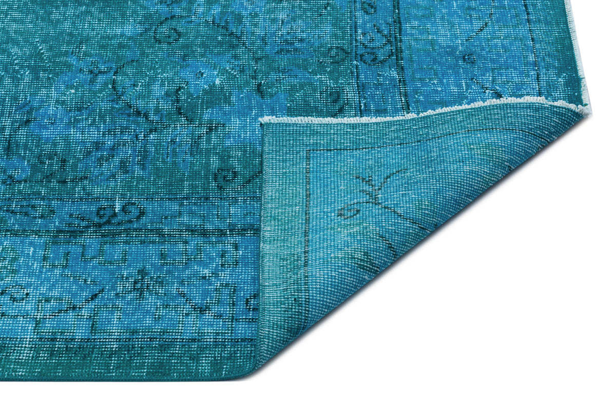 Teal distressed area rug with a faded traditional medallion pattern, shown with a corner folded over on white.