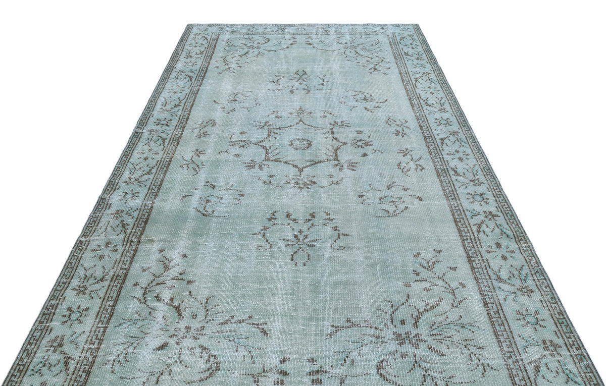 Light blue distressed rug with a central brown floral medallion and a decorative border on a white background.