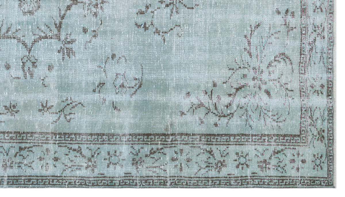 Light blue distressed rug with a faded brown floral pattern and a geometric border.