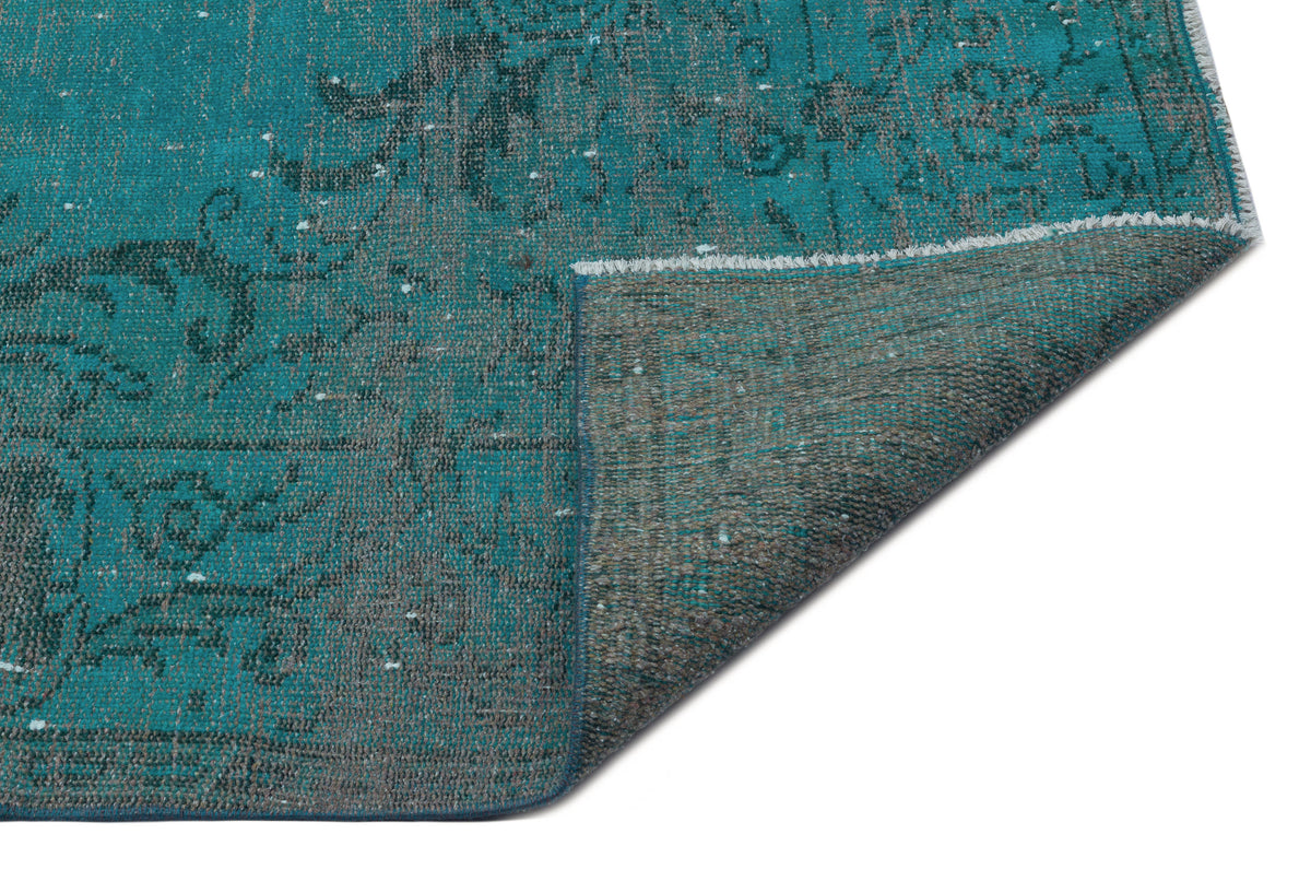 Teal and charcoal distressed rug with a traditional floral pattern, shown with a corner folded over.
