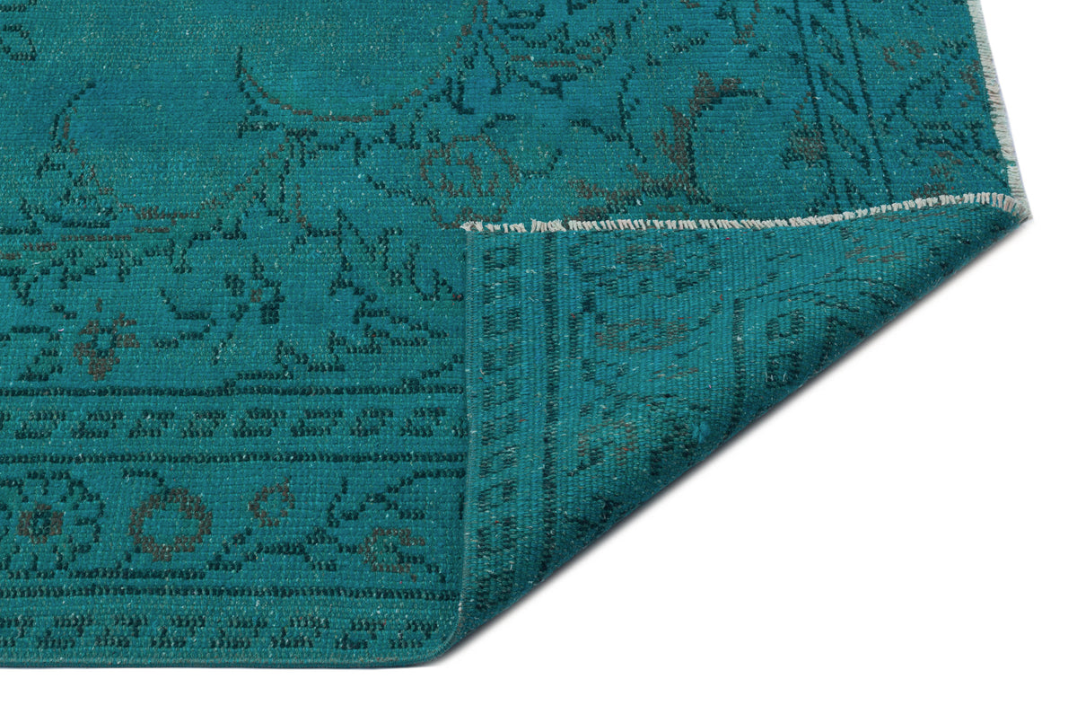 Teal rug with a dark grey distressed floral pattern, shown with a folded corner on a white background.