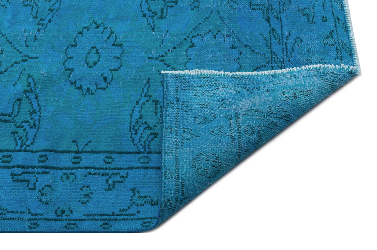 Bright blue rug with a distressed floral medallion pattern and a folded corner showing the underside.