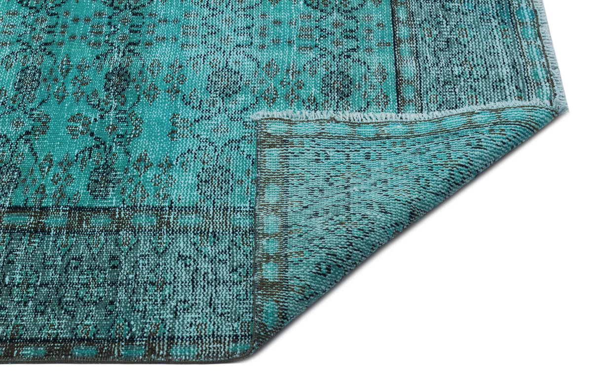 Turquoise and charcoal distressed rug with a traditional floral medallion pattern, shown with a folded corner.