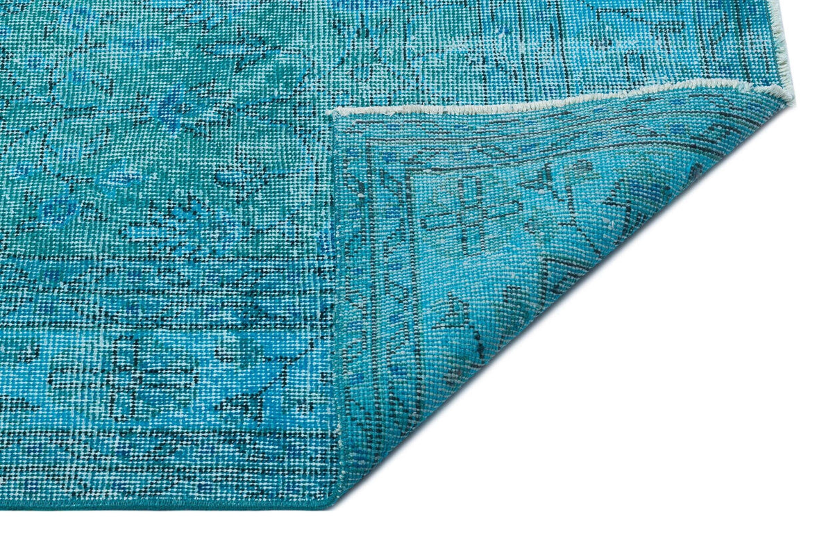 Turquoise and blue distressed rug with a traditional medallion pattern, shown with a folded corner on a white background.