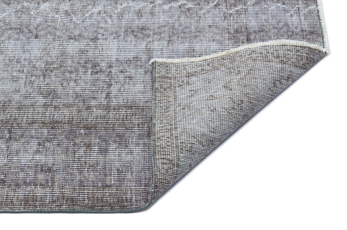 Grey and white distressed traditional rug with a faded medallion pattern, shown with a corner folded over.