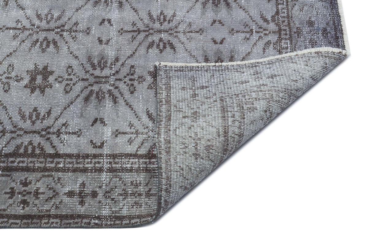 Grey and charcoal distressed rug with a geometric diamond and floral pattern, shown with a folded corner.