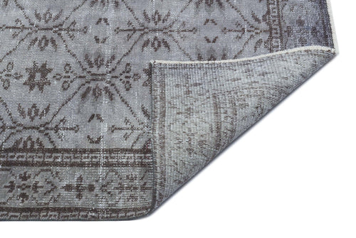 Load image 1 in gallery view. Grey and charcoal distressed rug with a geometric diamond and floral pattern, shown with a folded corner.