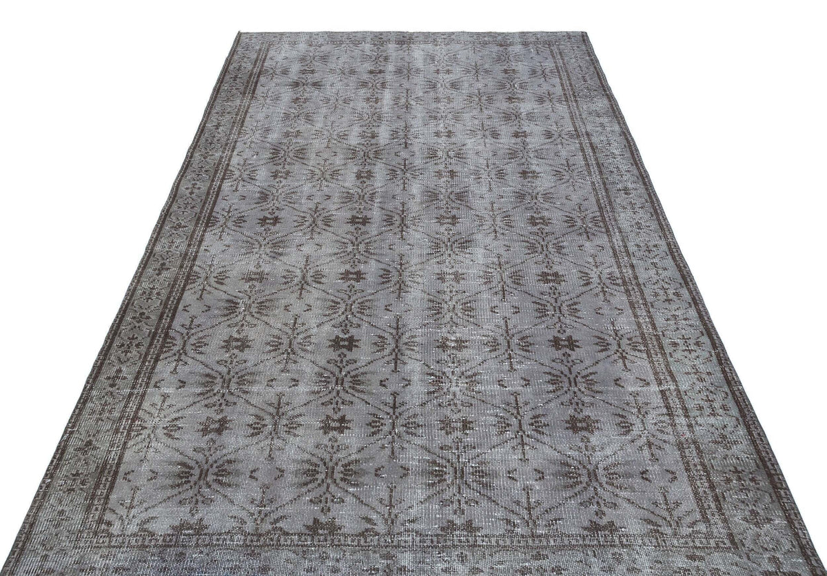 Grey and brown distressed rug with a repeating geometric floral lattice pattern and a wide decorative border.
