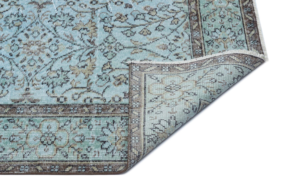 Light blue and brown traditional floral medallion rug with a folded corner showing the underside on a white background.