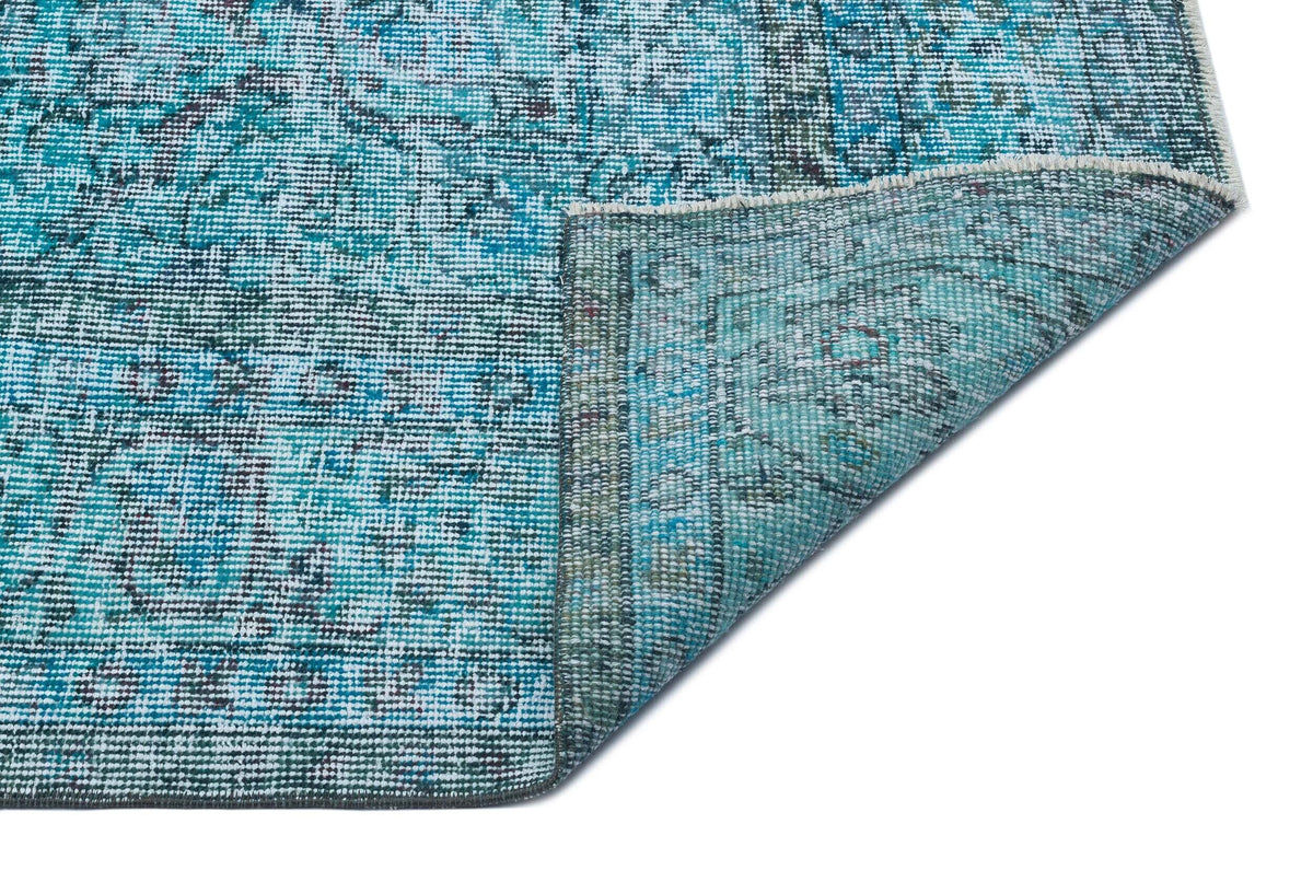 Distressed turquoise and teal area rug with a traditional medallion pattern, shown with a corner folded over.