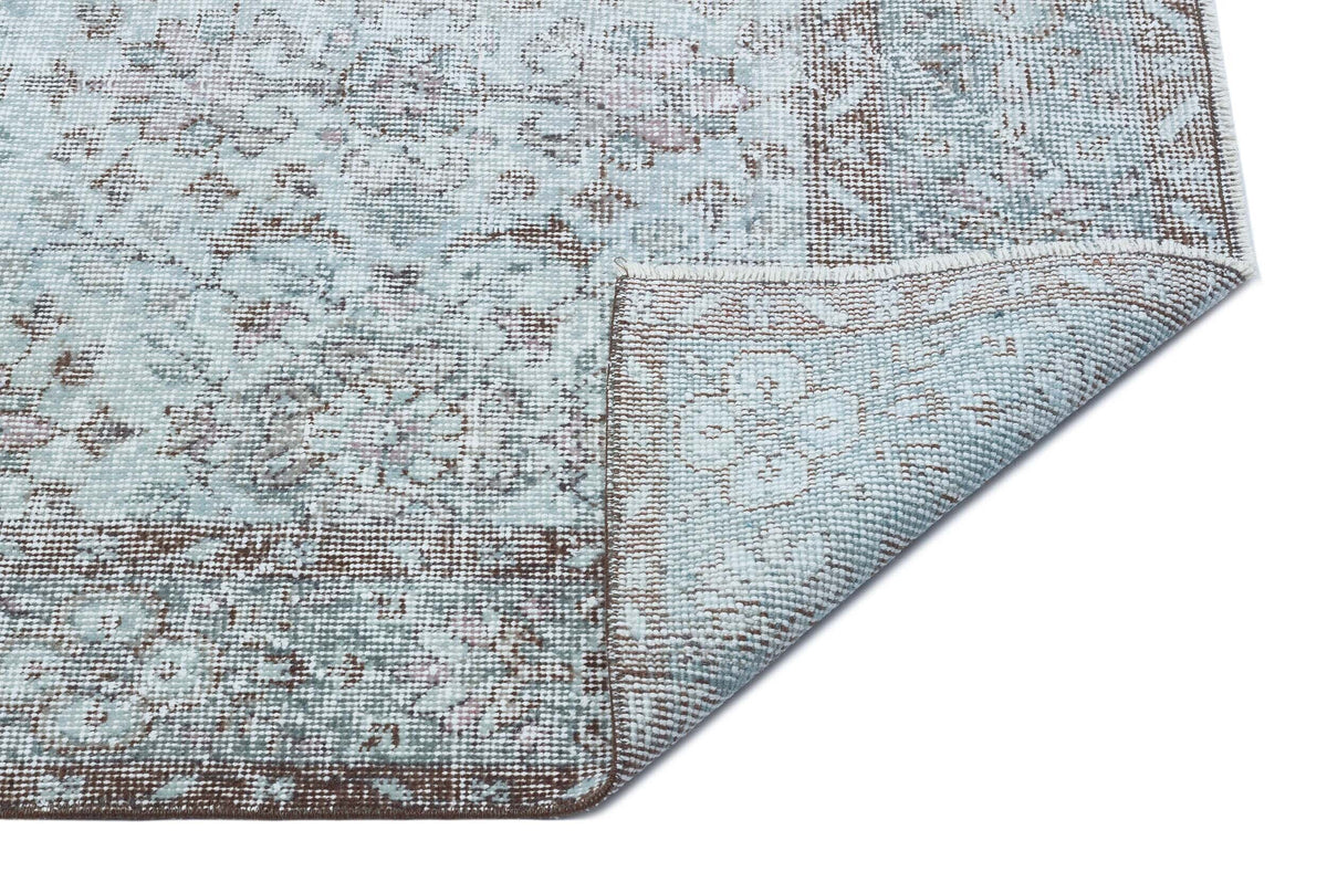 Light blue and brown distressed traditional rug with a floral medallion pattern, shown with a corner folded over.