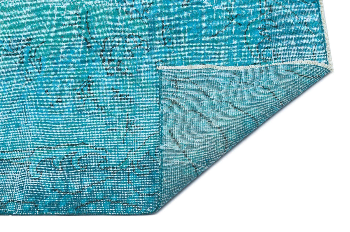 Bright turquoise distressed rug with a faded black floral pattern and a folded corner showing the underside.